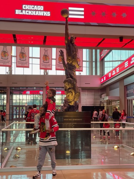 Me carrying my son on my shoulders in the United Center concourse, with the Michael Jordan statue.
