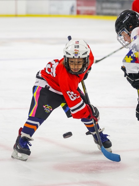My taking a face off in a red Pucks for Autism jersey, eyes locked on the puck.